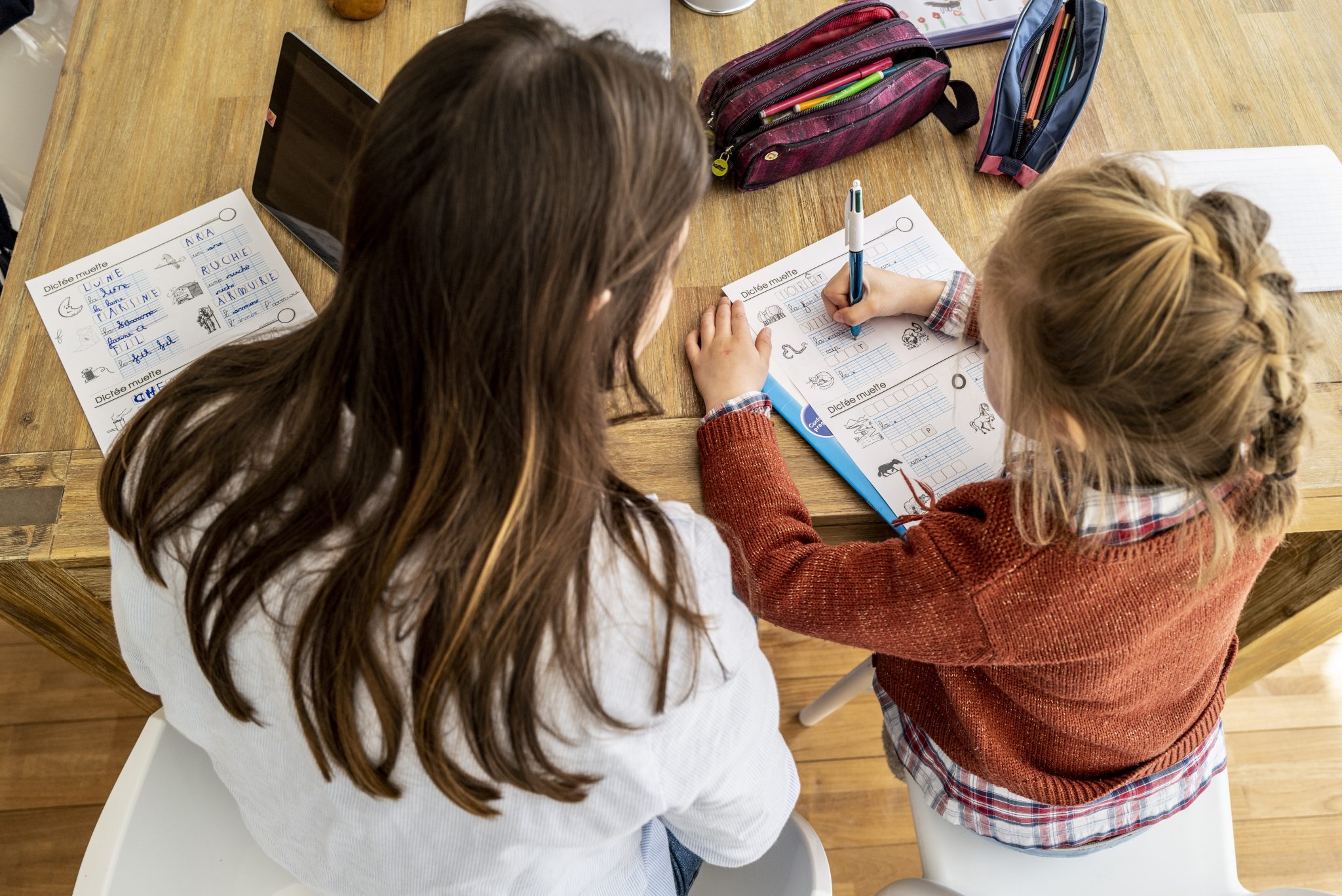 On y voit une femme et un enfant devant une table sur laquelle est posé du matériel d'écriture. Ils sont en train de remplir ensemble un questionnaire. Nous soutenons les enfants dans nos crèches autant que nécessaire, sans toutefois oublier la formation de leur autonomie.
