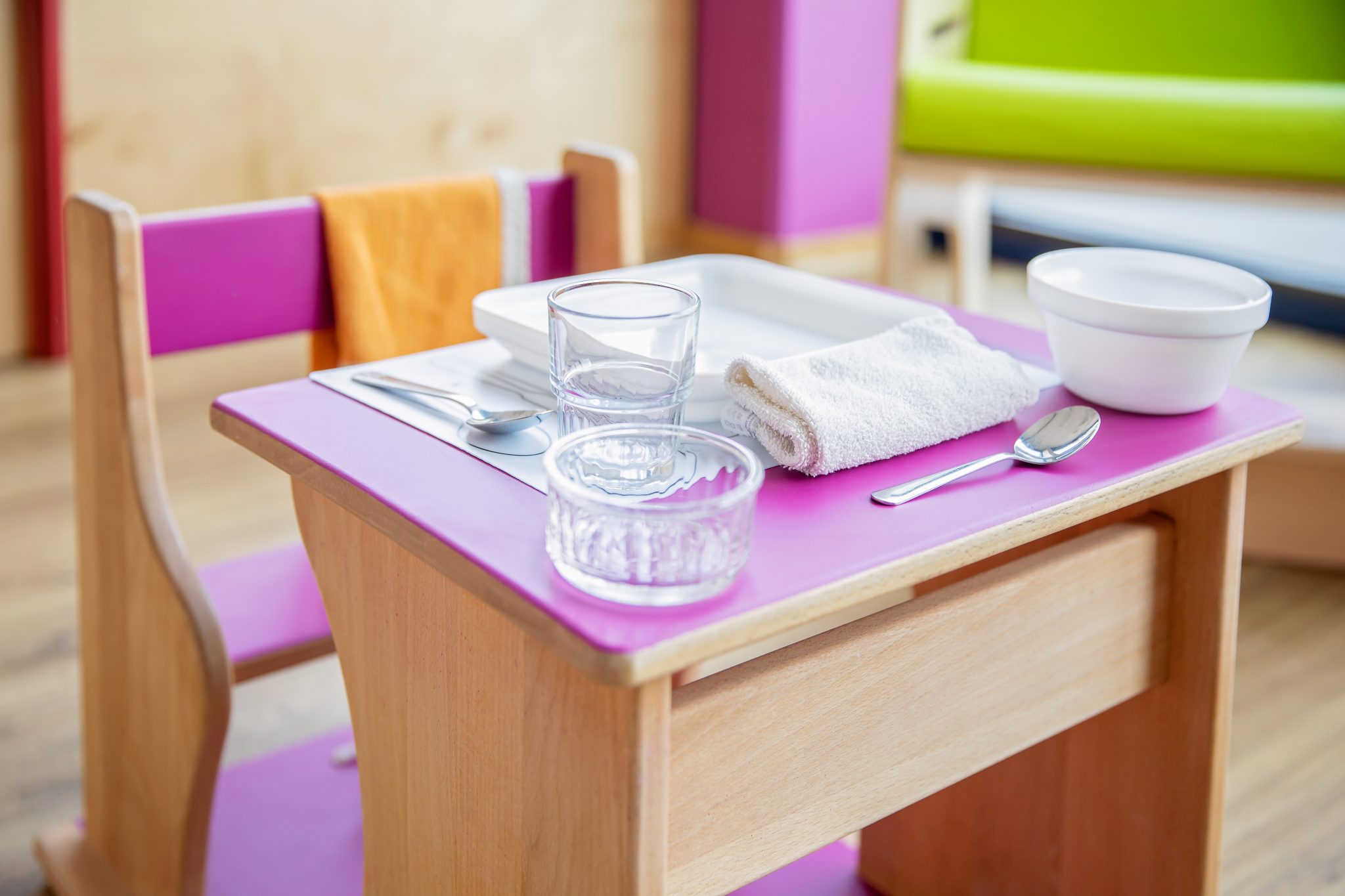 Sur cette photo, on peut voir un banc Pikler, en bois comme tous les meubles Pikler. Il contient une assiette, des couverts, un verre, une serviette et un bol. Grâce à la méthode Pikler, nous encourageons le développement de l'autonomie. De plus, nous plaçons une alimentation équilibrée au cœur du quotidien des enfants de nos crèches.