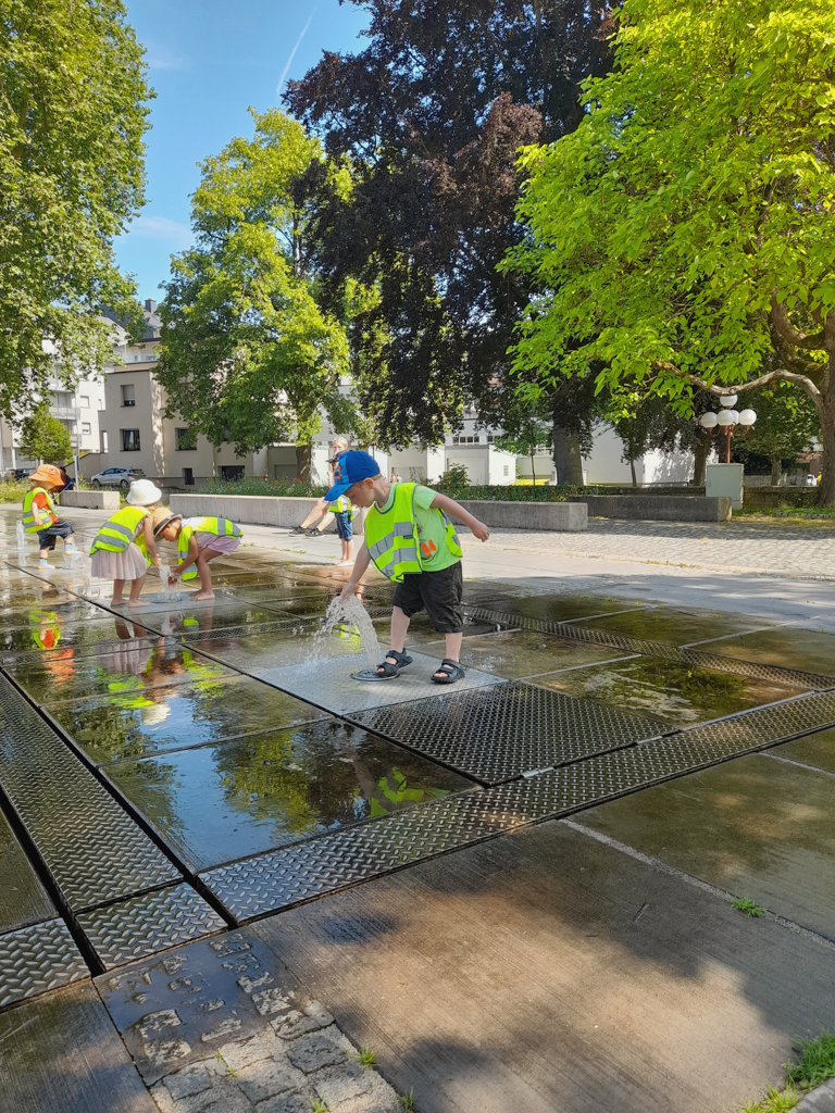 Cinq enfants jouent ensemble dans une cour intérieure avec de l'eau sur des dalles de pierre. De telles activités favorisent la vie sociale et préparent les enfants de nos crèches à leur future vie en société.