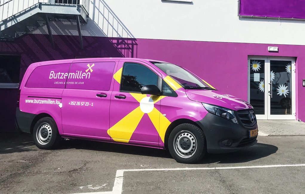 On y voit une camionnette aux couleurs de Butzemillen et un grand logo imprimé. Pour que les enfants puissent pratiquer leurs loisirs et autres activités extrascolaires pendant que les parents travaillent, nous proposons le transport depuis nos crèches.