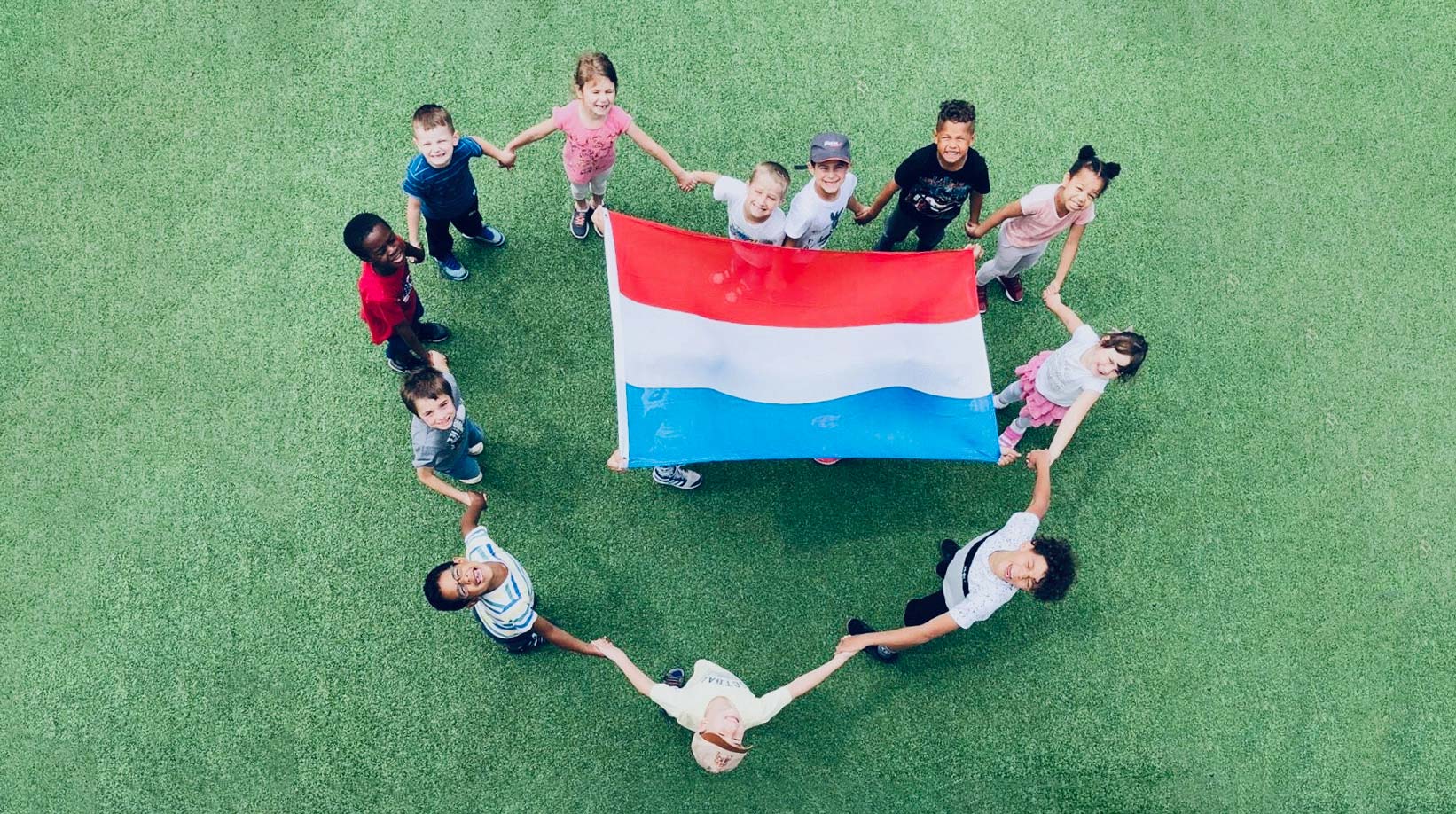Un groupe d'enfants se trouve en forme de cœur autour du drapeau luxembourgeois. L’image représente les nombreuses fêtes qui sont célébrées dans nos crèches. En plus des fêtes traditionnelles comme la Saint-Nicolas, nous avons notre propre fête, le Butzefest. Chaque dernier jeudi du mois a lieu le Celebration Day. Ces fêtes contribuent à renforcer la cohésion du groupe et offrent la possibilité de nouer de nouveaux contacts et de nouvelles amitiés.