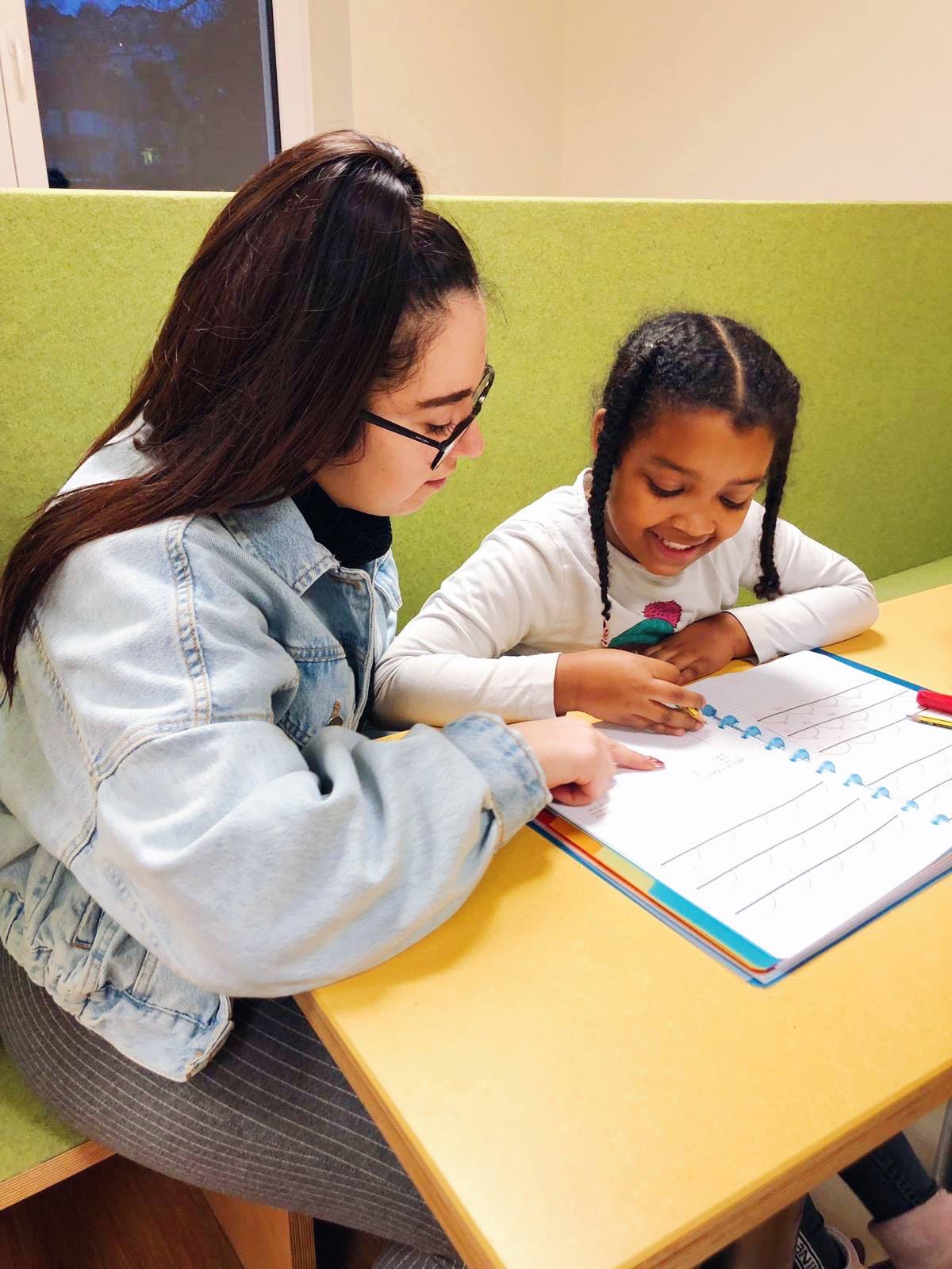 Une femme est assise à côté d'un enfant qui est penché sur un cahier. Les devoirs de nos crèches préparent les enfants à la rentrée scolaire. En donnant aux enfants des devoirs à domicile, nos crèches impliquent les parents dans l'éducation et nous aident à préparer les enfants à leur scolarité. D'autre part, les enfants ont ainsi la possibilité de partager leur expérience avec leurs parents.