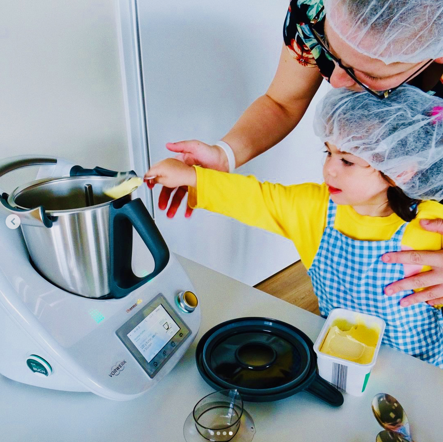 Une femme se tient au-dessus d'un enfant qui saisit un appareil de cuisine. On voit également un paquet de magarine. Les enfants sont impliqués avec nos éducateurs dans des tâches quotidiennes comme la préparation des repas, ce qui leur permet d'apprendre très tôt à prendre des responsabilités et les prépare à leur vie future.